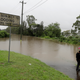 Three men shelter under an umbrella near a flooded road as rain falls in Windsor, northwest of Sydney.